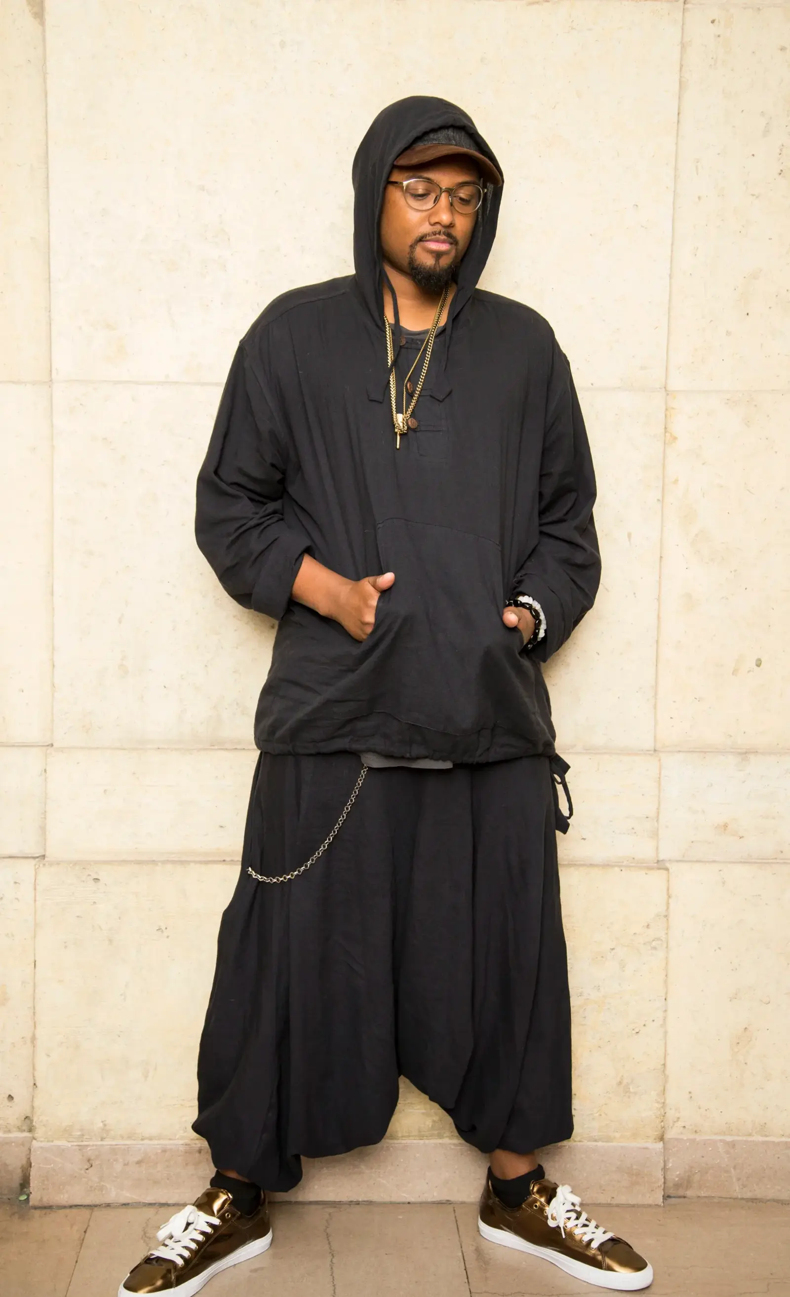 The Broken Wings founder in an all-black hooded look against a stone wall.